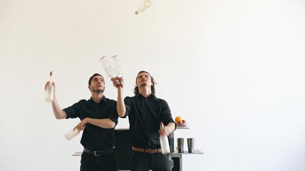 Professional bartender men juggling bottles and shaking cocktail at mobile bar table