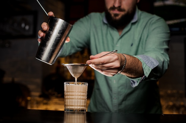 Professional bartender pours alcohol from the shaker