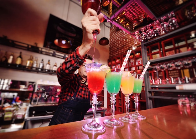 Professional bartender prepares and mixes cocktails pouring red syrup from a bottle 