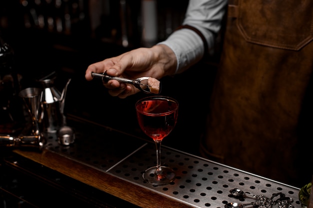 Professional bartender putting a rose bud to the red cocktail in the glass