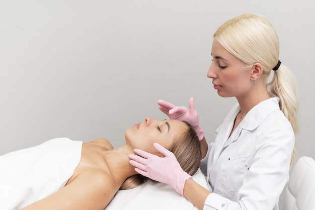 Professional beautician applies white cosmetic cream to a girl lying on a couch in a modern spa