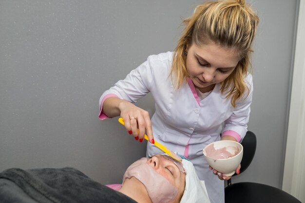 Foto estetista professionista che applica maschera alginato sul viso al salone della donna