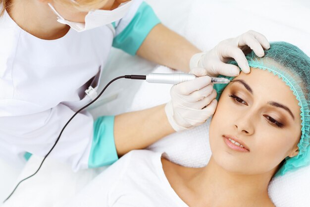 Professional beautician doing eyebrow tattoo at woman face. Permanent brow makeup in beauty salon, closeup. Cosmetology treatment.