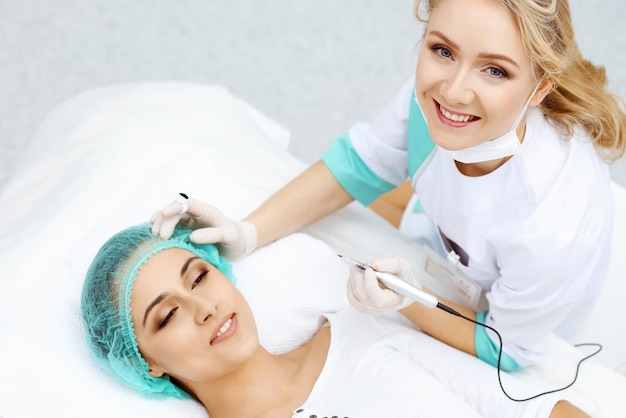 Professional beautician doing eyebrow tattoo at woman face. Permanent brow makeup in beauty salon, closeup. Cosmetology treatment.