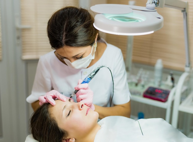 Professional beautician doing eyebrow tattoo at woman face permanent eyebrow makeup in beauty salon cosmetology treatment