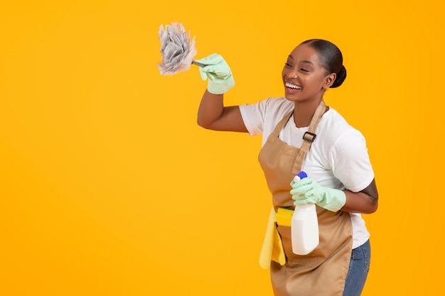 Professional black cleaner woman dusting copy space over yellow background