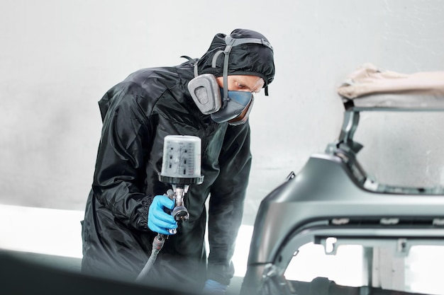 Photo in a professional body shop a man uses a respirator while applying a fresh coat of paint to a customers beloved car