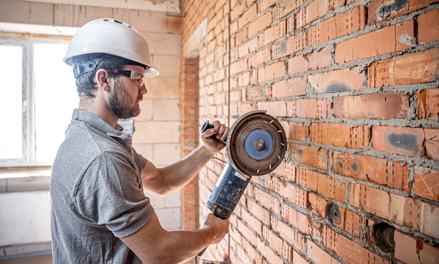 A professional builder in work clothes works with a cutting tool.