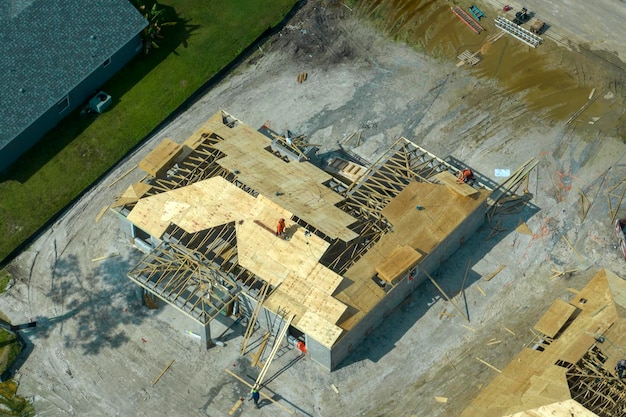 Professional builders working on roof construction of unfinished suburban home with wooden frame structure in Florida rural area Concept of housing development in America