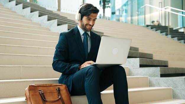 Professional business man sitting at stairs while working on laptop Exultant