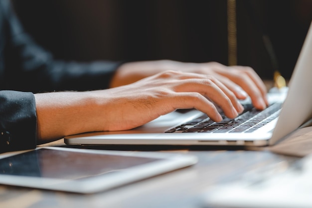 L'uomo d'affari professionista sta lavorando nella comunicazione del piano di lavoro di marketing online con il laptop utilizzando una mano per digitare la tastiera del computer nel moderno posto di lavoro dell'ufficio o nello spazio di coworking