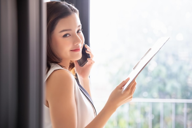 Foto donna d'affari professionale che utilizza lo smartphone tecnologico con appunti in possesso che guarda e sorride alla fotocamera concetto di lavoro da casa