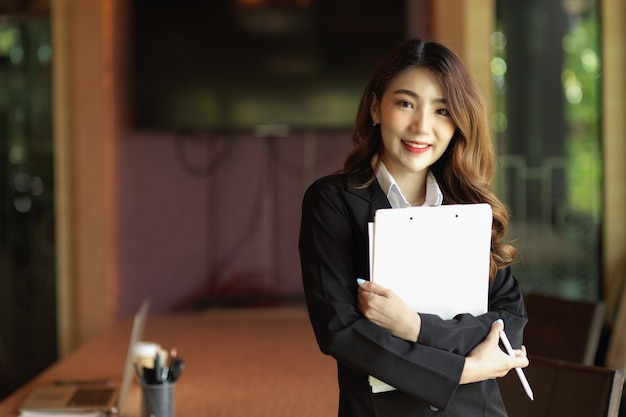 Professional businesswoman hold clipboard in her hands at office blur office room in the background