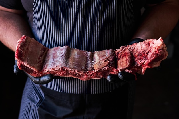 Professional butcher in a striped apron holds a large fresh cut of raw beef ribs showcasing the qual