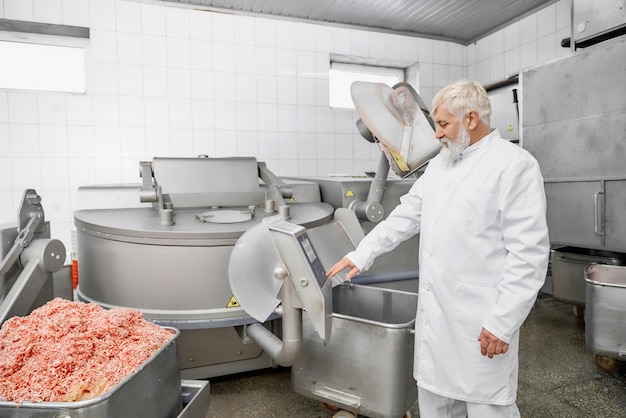 Professional butcher in uniform near equipment for meat.