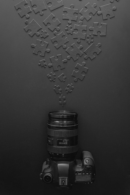 Photo professional camera lies on a black background next to black puzzles that accumulate to the camera lens