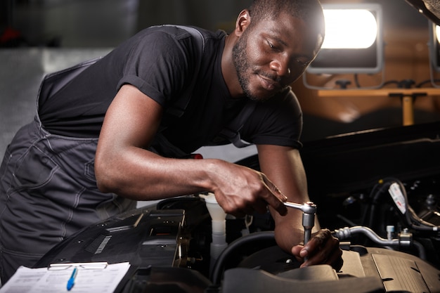 Professional car mechanic is examining engine under the hood at auto repair shop