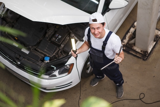 Meccanico professionista che sorride alla telecamera mentre ripara un'auto in officina