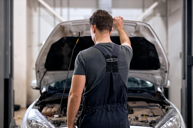 Foto meccanico professionista che lavora sotto il cofano dell'auto nel garage di riparazione chiudendo o aprendo il cofano