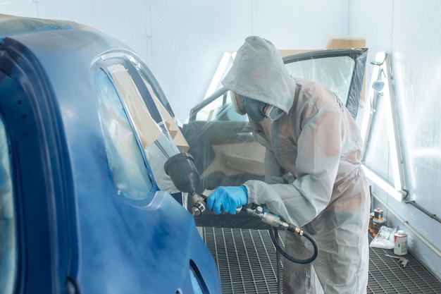 Professional car painter is painting in garage by airbrush.