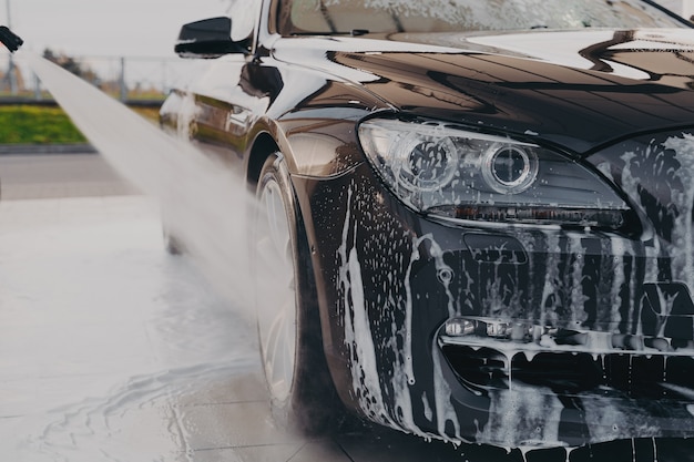 Professional car wash spraying water from high pressure washer to rinse off suds