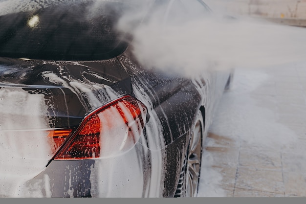 Professional car wash with high pressure washer and cleansing foam outdoors