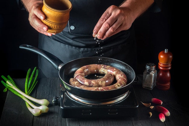 Lo chef professionista aggiunge sale alla padella con salsiccia di carne cruda preparazione per la cottura di salsicce