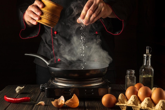 Professional chef adds salt while cooking eggs or an omelet in pan