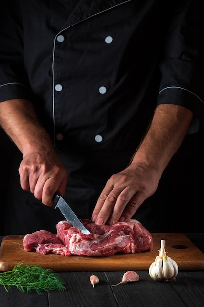 Professional chef cuts meat with a knife in the kitchen prepares food Vegetables and spices on the kitchen table in a restaurant to prepare a delicious lunch