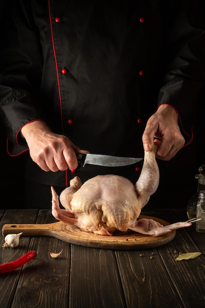 A professional chef cuts raw chicken with a knife in the kitchen