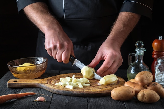 Professional chef cuts raw potatoes into pieces with a knife before preparing breakfast or dinner