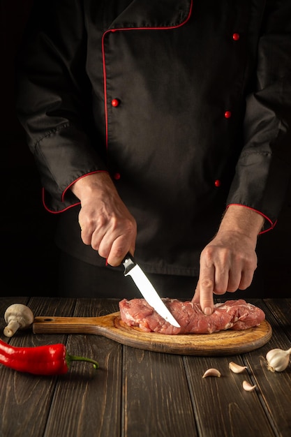 A professional chef cuts raw veal meat on a cutting board\
before baking