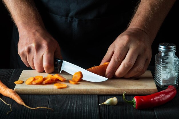 Professional chef is cutting carrots for vegetable soup in the restaurant kitchen