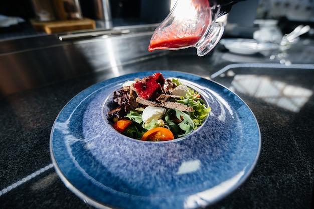 A professional chef prepares a delicious fresh salad of green vegetables and juicy veal in a modern and stylish restaurant. Cooking in a restaurant.