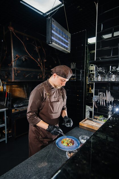 Uno chef professionista prepara una deliziosa insalata fresca di verdure verdi e succosa carne di vitello in un ristorante moderno ed elegante. cucinare in un ristorante.