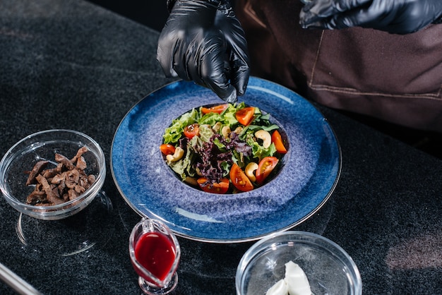 A professional chef prepares a delicious fresh salad of green vegetables and juicy veal in a modern and stylish restaurant