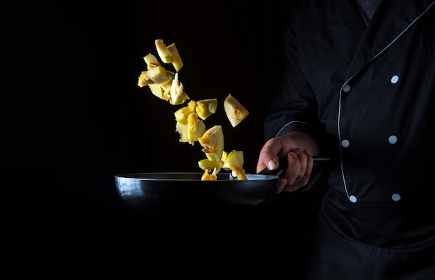 プロのシェフがズッキーニを鍋で調理します。暗い背景で野菜の健康的な菜食主義の食糧および食事を調理します。無料の広告スペース