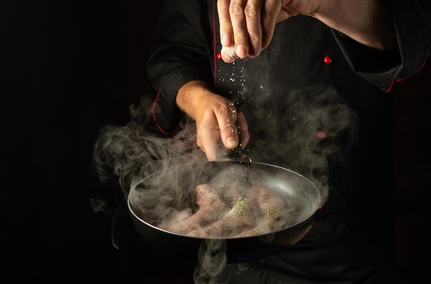 Professional chef salts meat sausages in a hot pan with steam