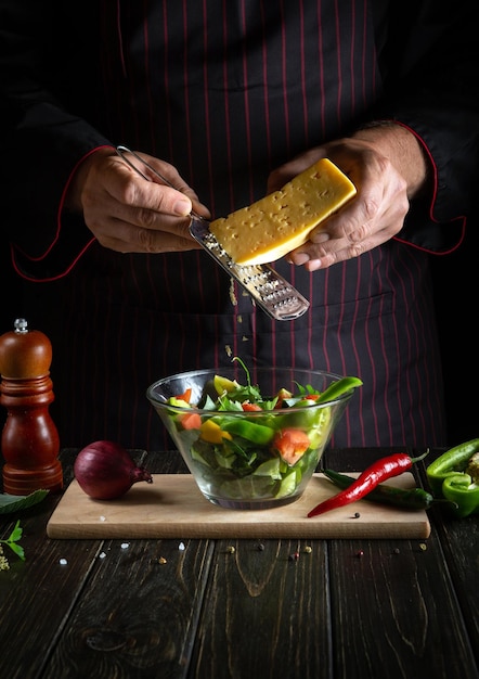 Professional chef sprinkles cheese on a salad of fresh vegetables in a plate