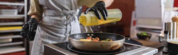 The professional chef in uniform adds oil into pan with dish in restaurant kitchen