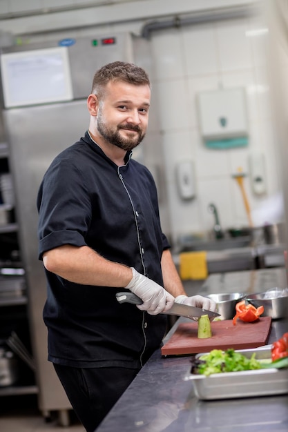 Профессиональный шеф-повар в униформе нарезает свежие овощи на кухне Повар готовит вкусный гарнир для клиентов в ресторане Кулинарная концепция