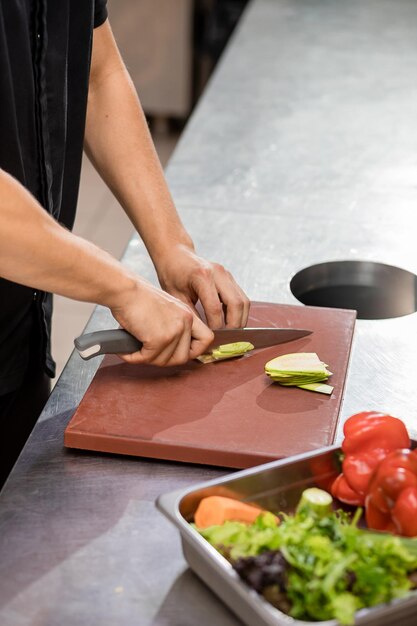 レストランのキッチンでまな板に新鮮な野菜を準備する制服を着たプロのシェフ料理のコンセプト