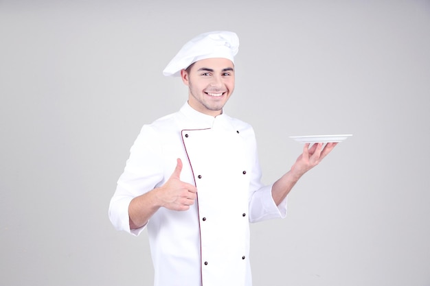 Professional chef in white uniform and hat on gray background