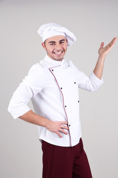 Professional chef in white uniform and hat on gray background