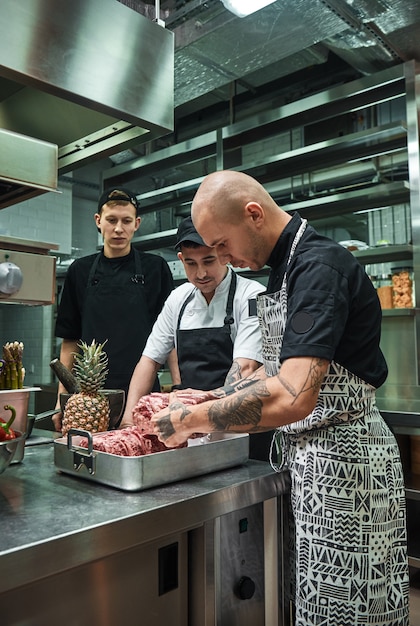 Chef professionista con tatuaggi sulle mani in possesso di una carne rossa e assistenti didattici