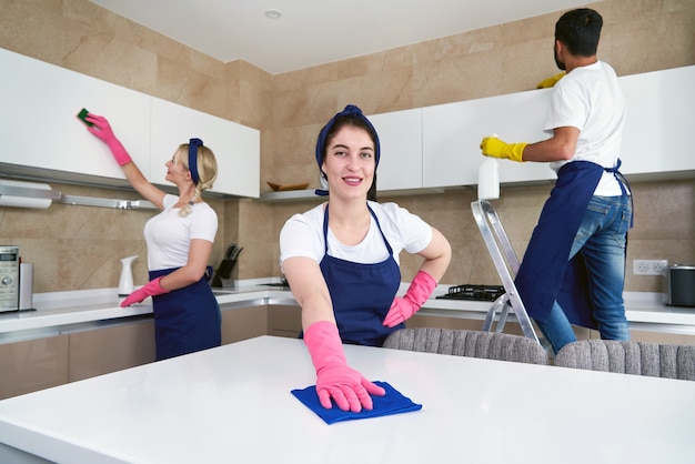 Professional cleaners in blue uniform washing floor and wiping dust from the furniture in the living room of the apartment. Cleaning service concept