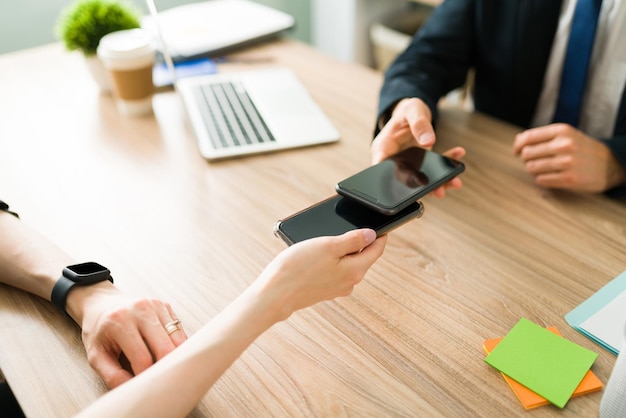 Professional colleagues exchanging their digital business cards and information contact by bringing the smartphones closer at the office desk