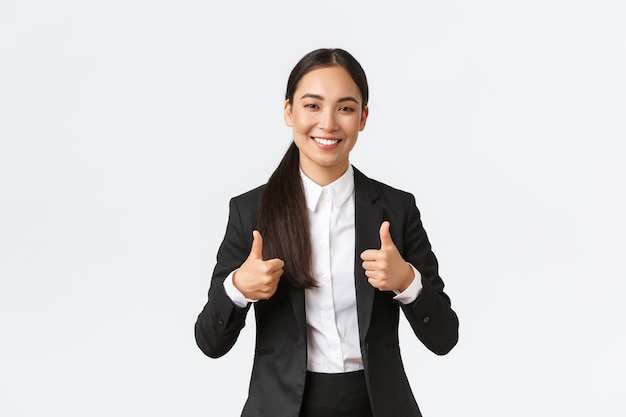 Professional confident smiling asian businesswoman assure everything going great, showing thumbs-up, recommend agency or product, like and approve, say well done, nice work or good job