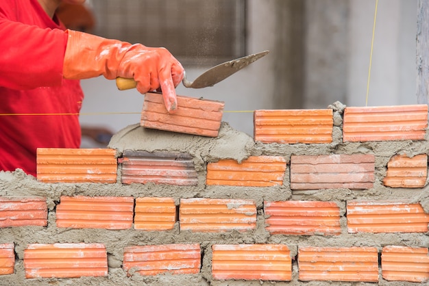 Professional construction worker laying bricks and building wall in industrial site. 