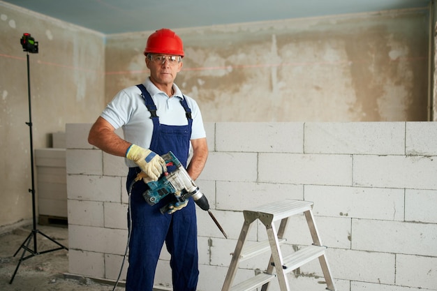 Professional construction worker in uniform standing with rotary hammer drill portrait of contractor